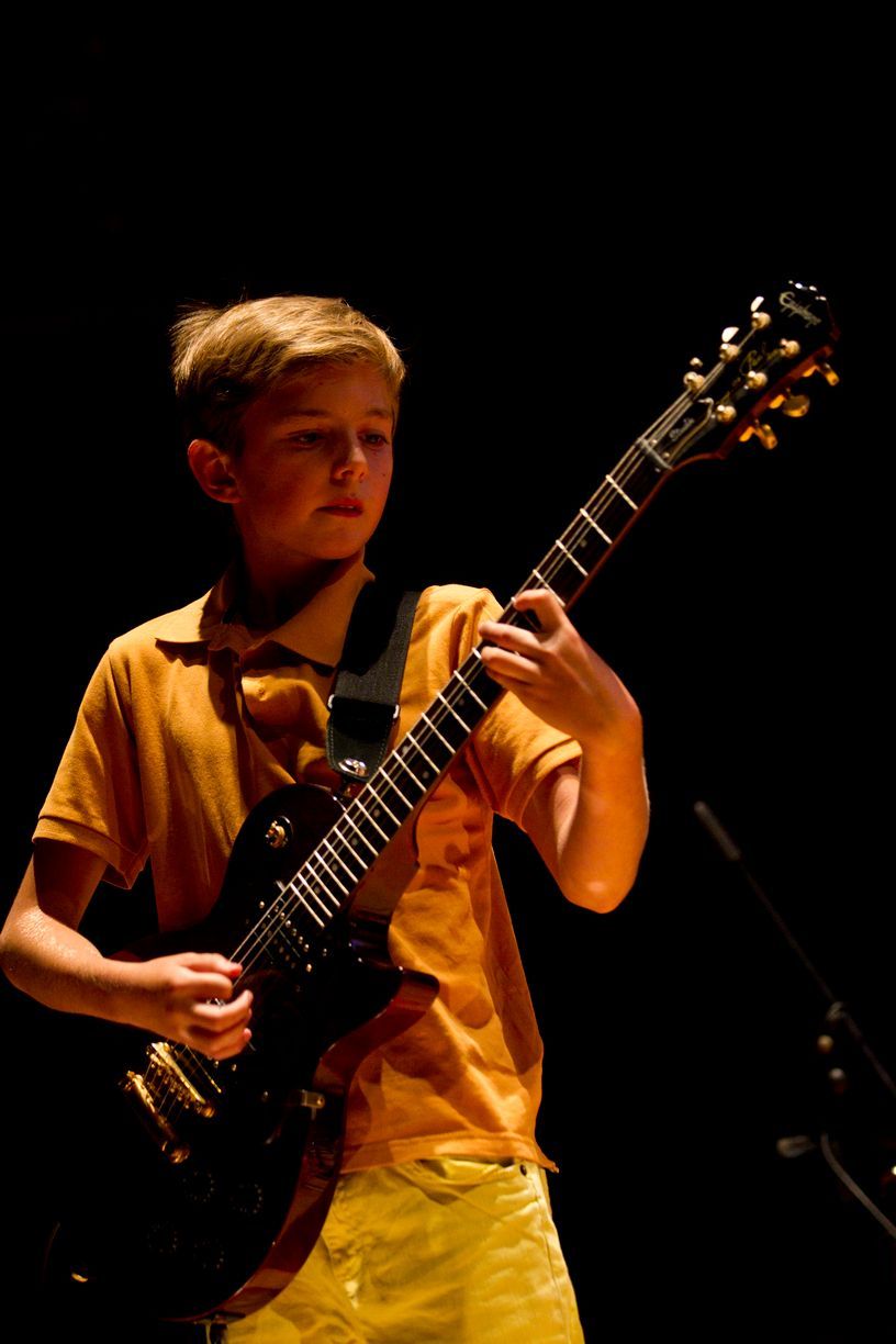 Un niño con una camisa amarilla está tocando una guitarra eléctrica.