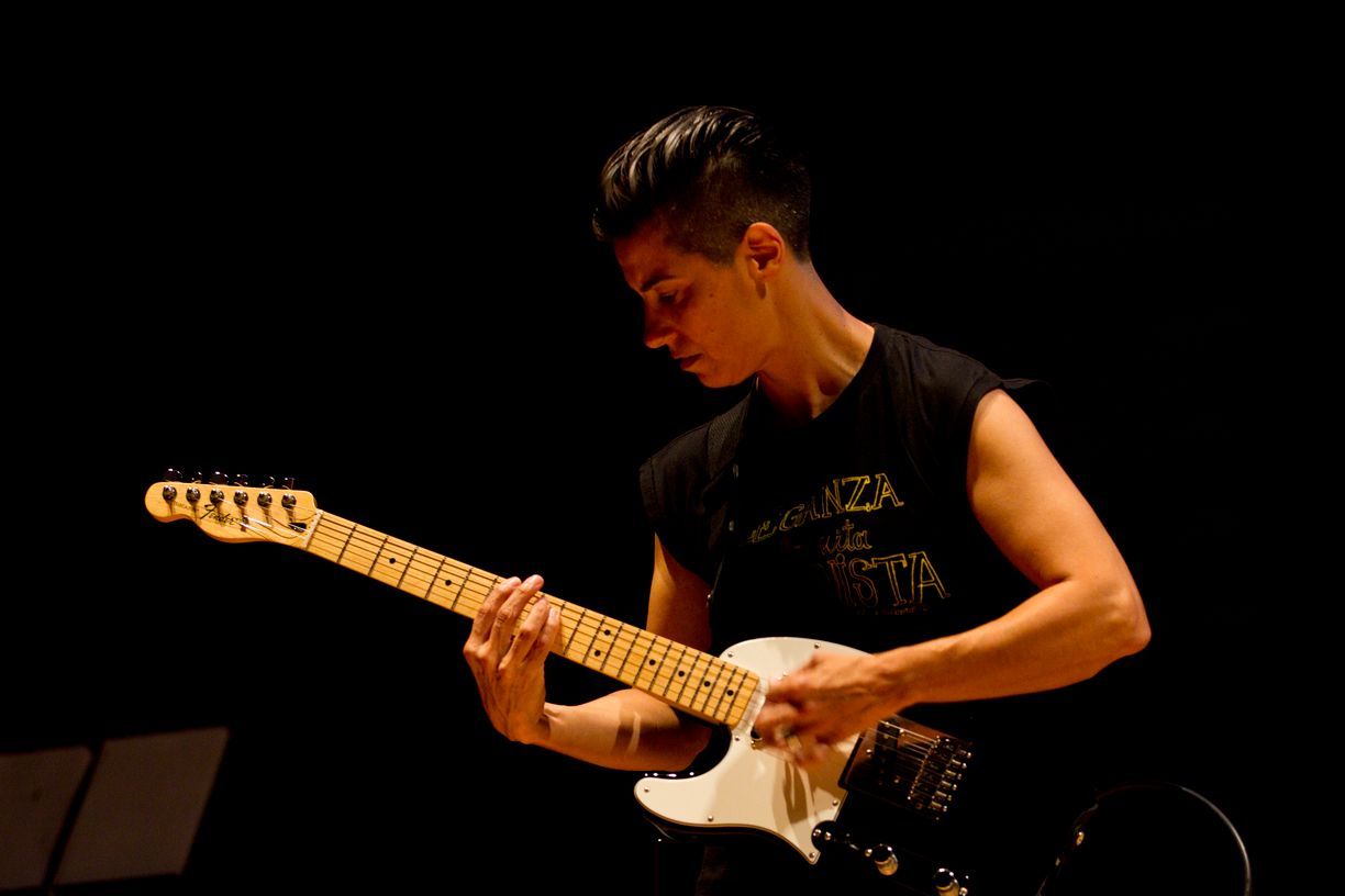 Un hombre está tocando una guitarra eléctrica en una habitación oscura.