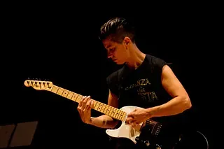 Un hombre está tocando una guitarra eléctrica en una habitación oscura.