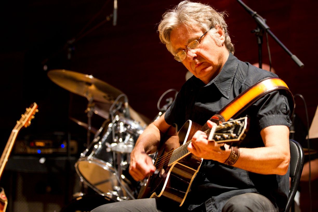 Un hombre está tocando una guitarra en un escenario delante de una batería.