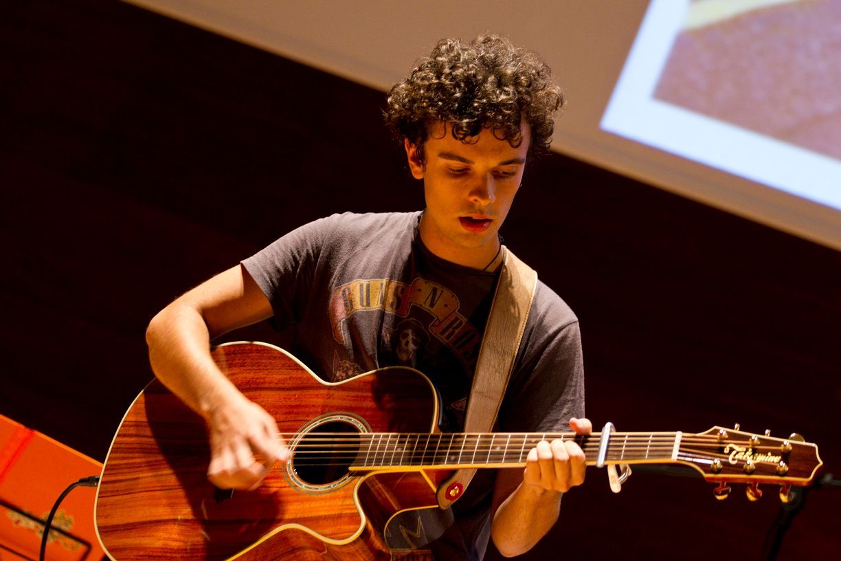 Un joven está tocando una guitarra acústica en el escenario.