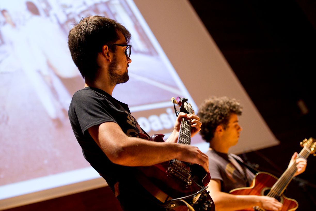 Dos hombres están tocando guitarras frente a una pantalla que dice bajo