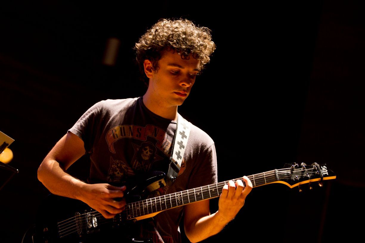 Un joven está tocando una guitarra en una habitación oscura.