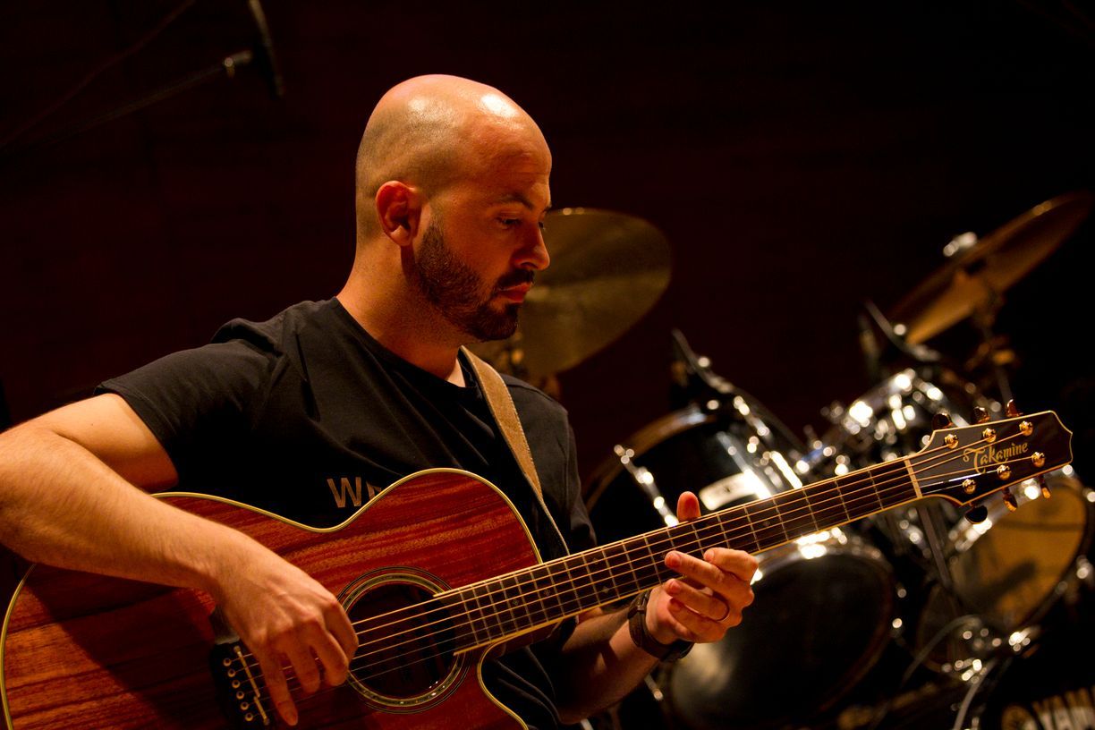 Un hombre con barba está tocando una guitarra acústica.