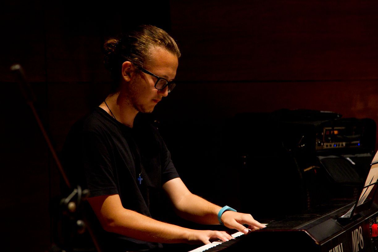 Un joven está tocando un teclado en una habitación oscura.