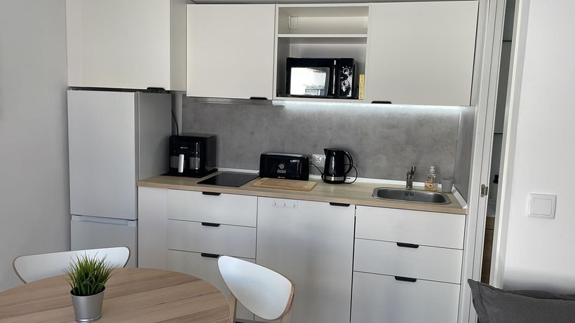 Una pequeña cocina con gabinetes blancos, una mesa y sillas.