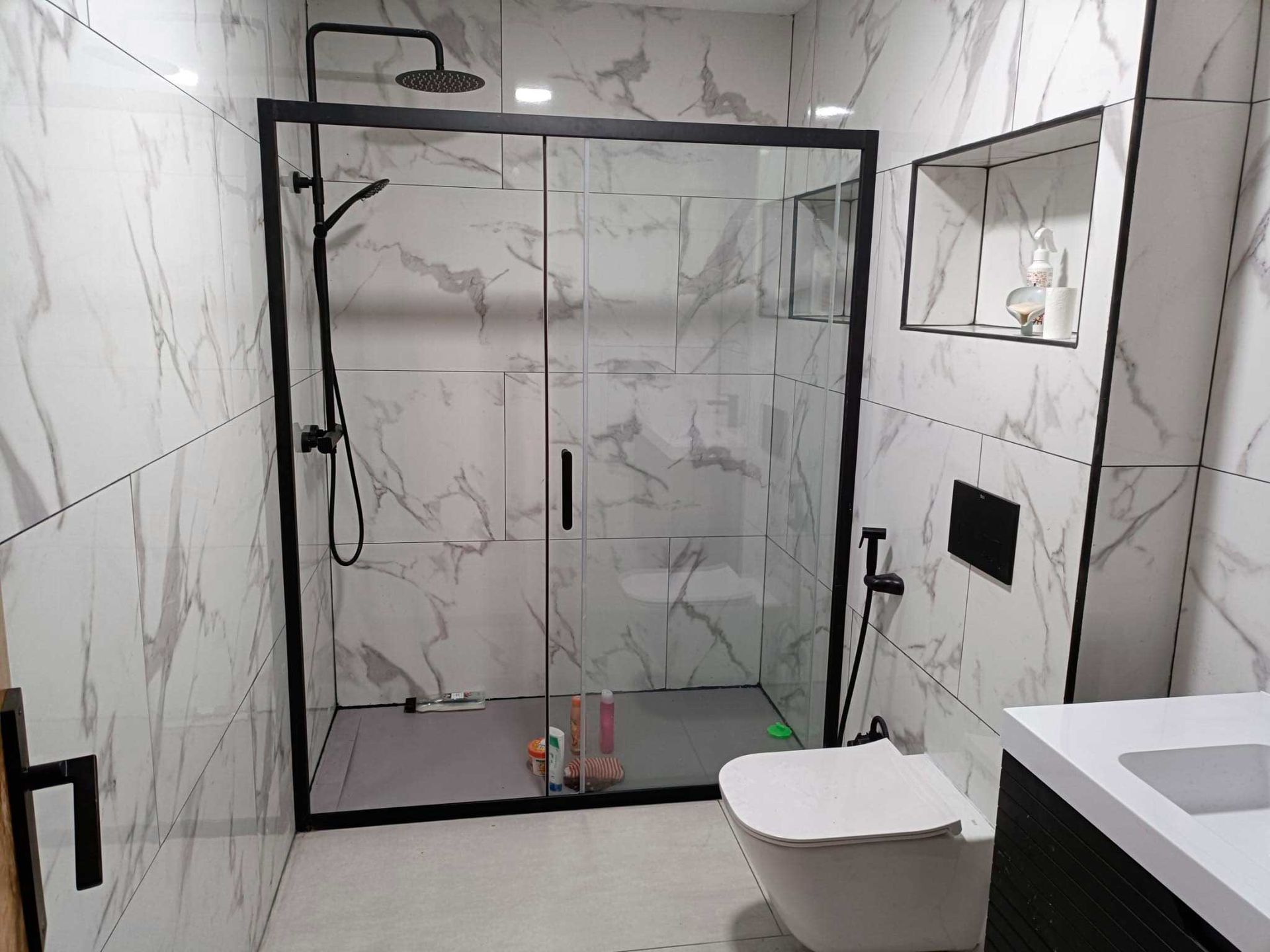 Un baño con azulejos blancos, un inodoro y una cabina de ducha.
