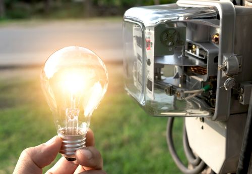 Una persona sostiene una bombilla delante de un medidor eléctrico.