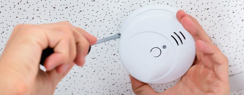Una persona sostiene un detector de humo con un destornillador.