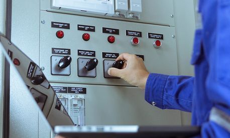 Un hombre está trabajando en un panel eléctrico mientras sostiene una tableta.