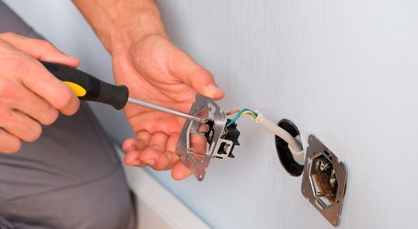 Un hombre está arreglando un tomacorriente eléctrico con un destornillador.