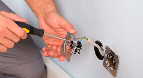 Un hombre está arreglando un tomacorriente eléctrico con un destornillador.