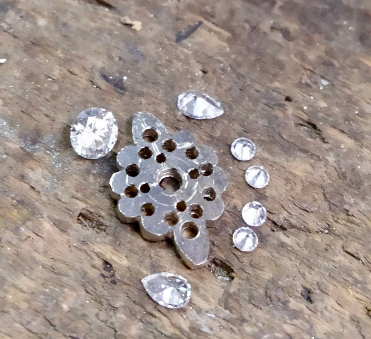 Pendentif en argent avec trous, entouré de diamants en vrac sur une surface en bois.