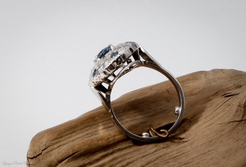 Bague avec pierres bleues et blanches sur bois sur fond blanc.