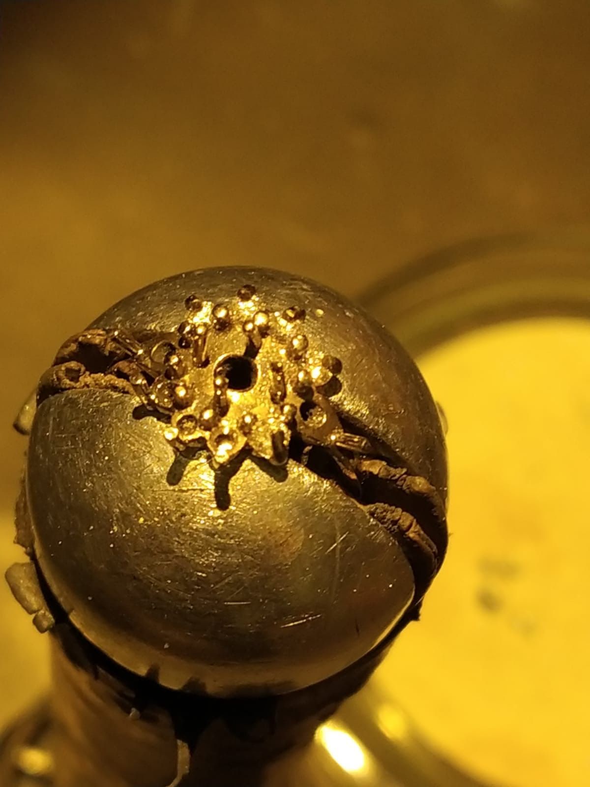 Sphère en métal de couleur dorée avec un design en forme d'étoile et une fente sur le côté, éclairée d'une teinte jaune.