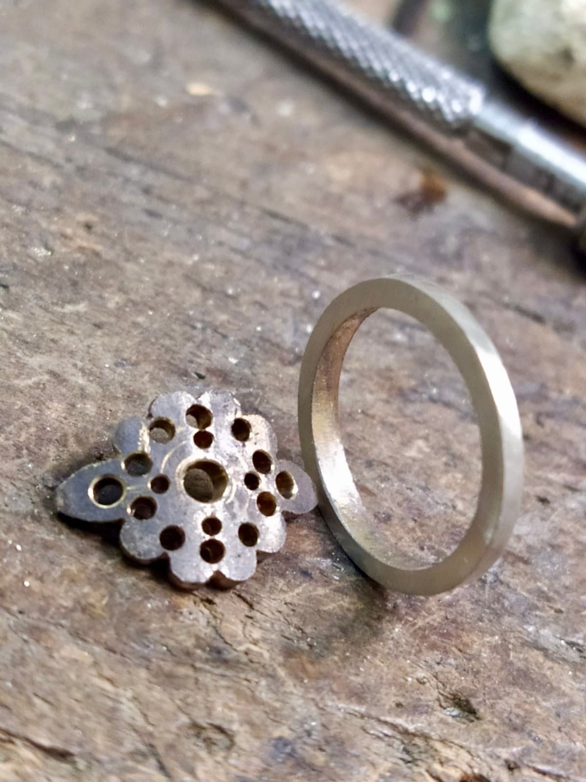 Bague en argent et pièce décorative en métal avec motif floral sur une surface en bois.