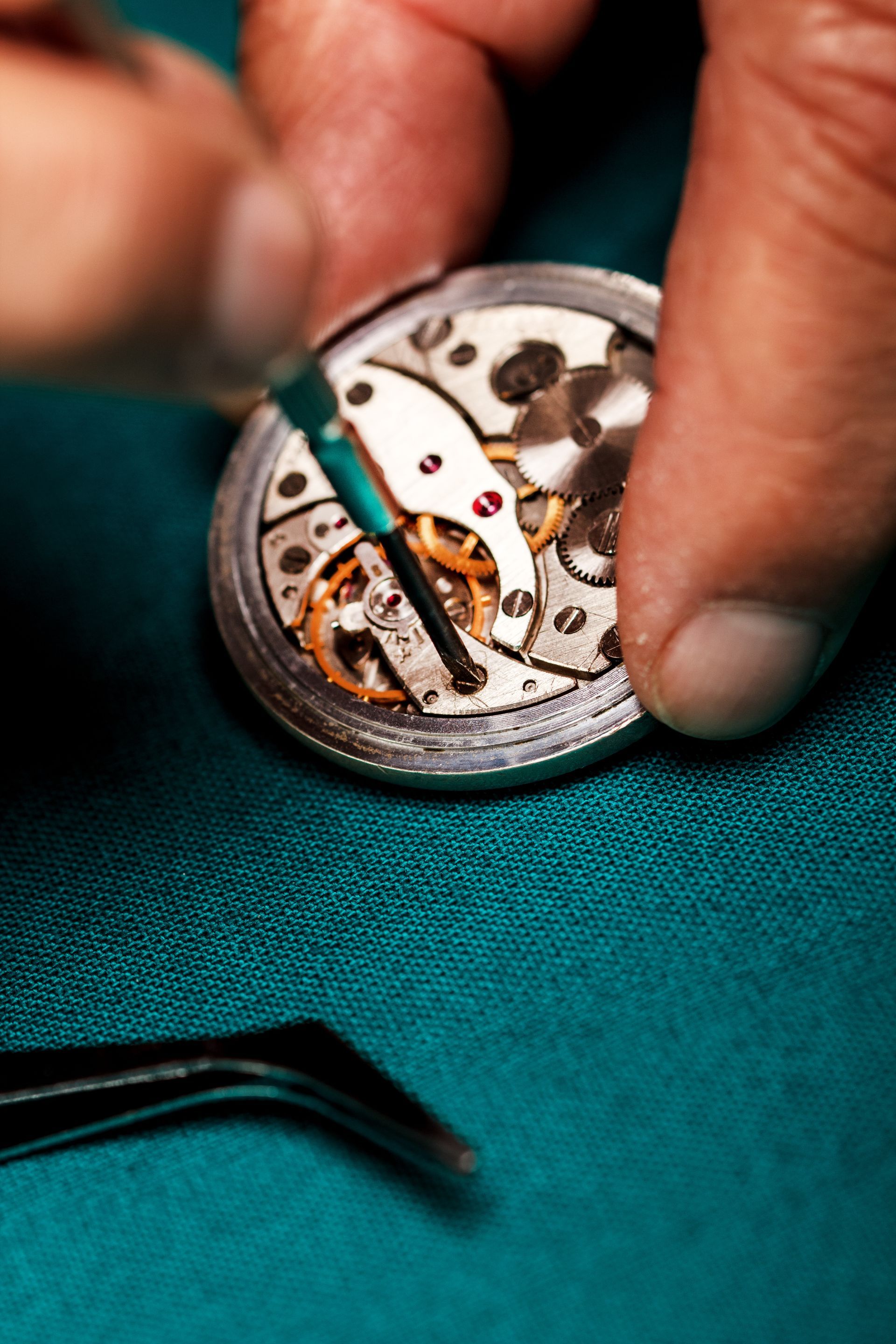 Mains travaillant sur des composants de montre avec des pincettes sur une surface verte.