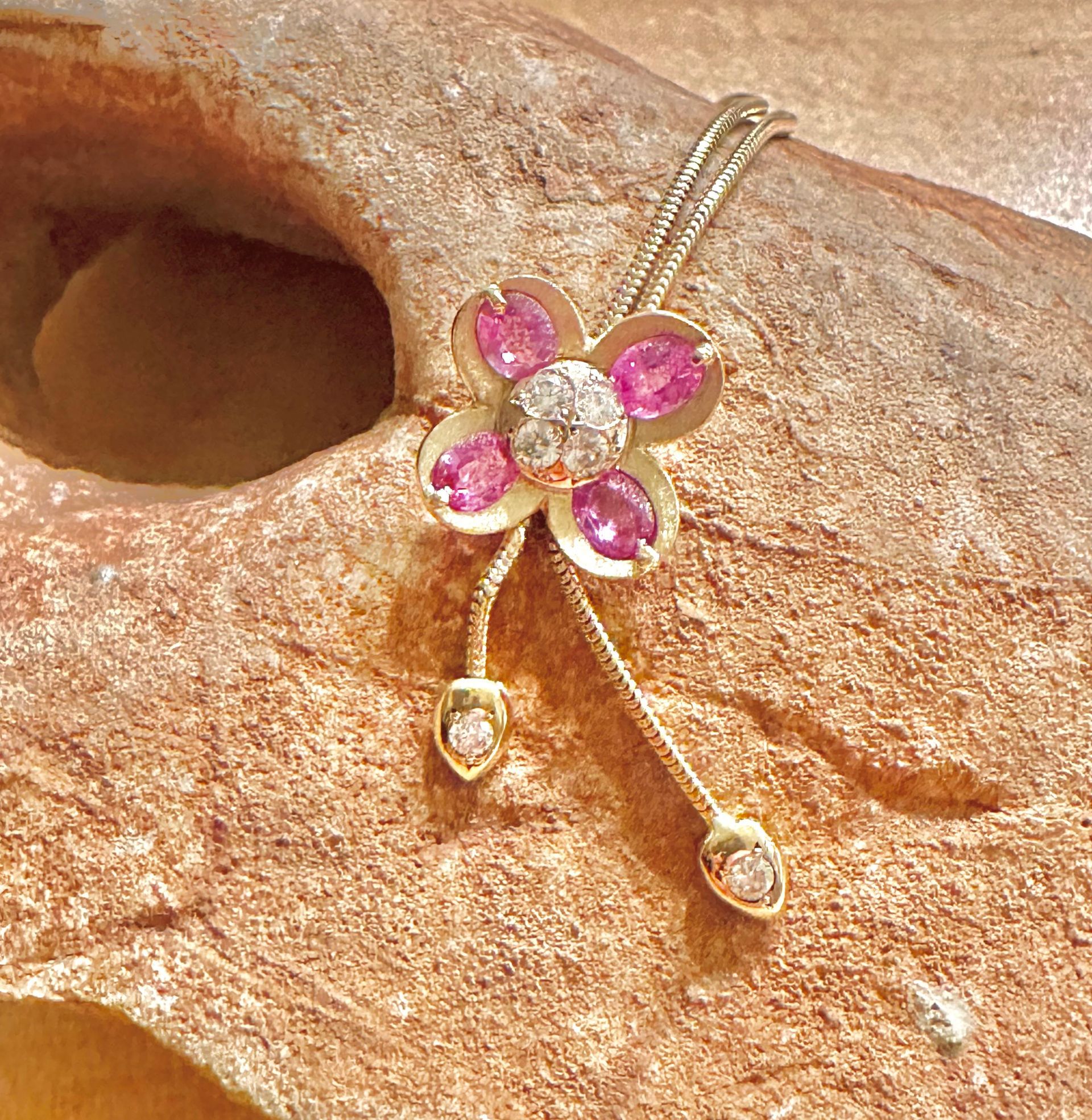 Collier pendentif fleur en or avec pierres roses et diamants sur un rocher.