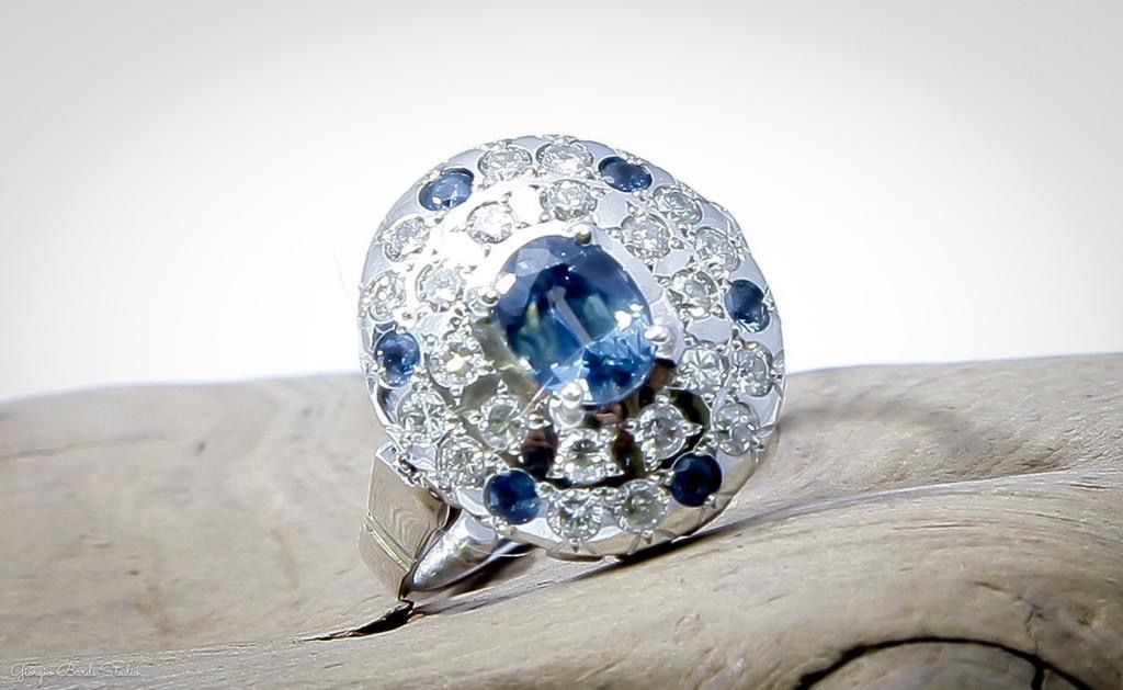 Bague ornée d'une gemme bleue entourée de pierres blanches et bleues, reposant sur du bois.