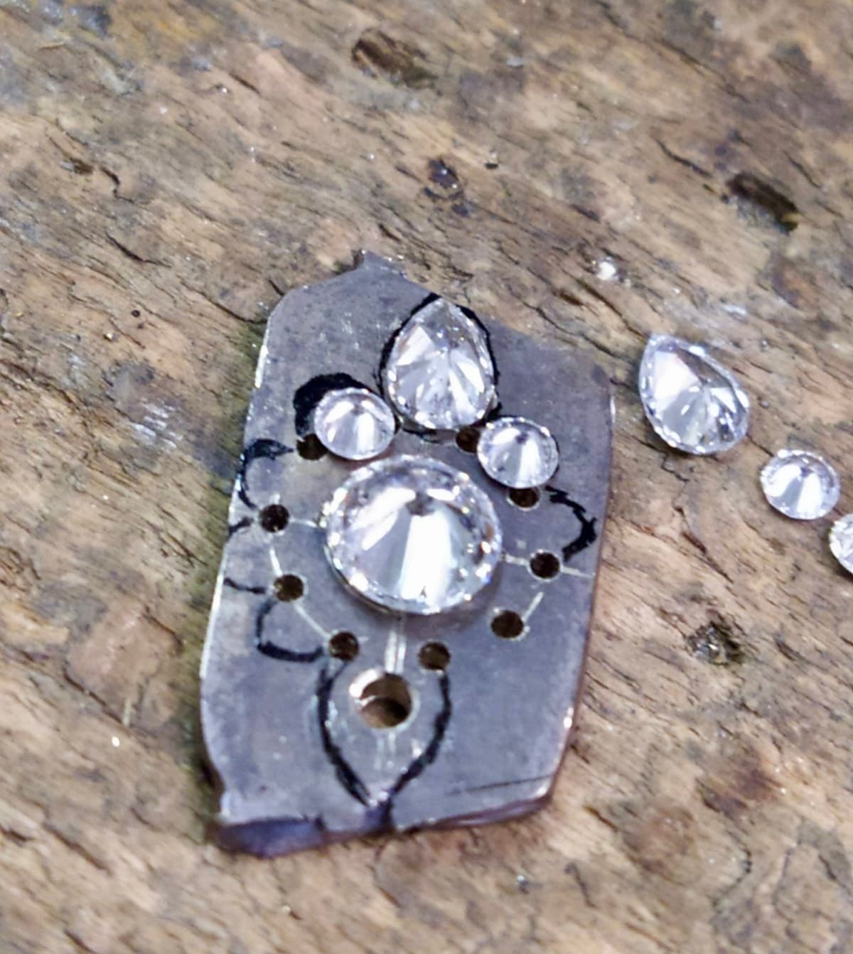 Un morceau de métal avec un motif dessiné et des diamants disposés dessus, prêt à être serti.