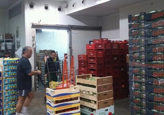 Un hombre empuja un carrito en una habitación llena de cajas de frutas y verduras.