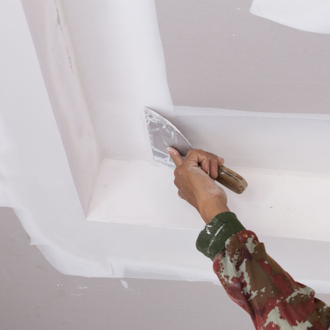 Une personne utilise une spatule à mastic pour appliquer du composé sur un plafond.