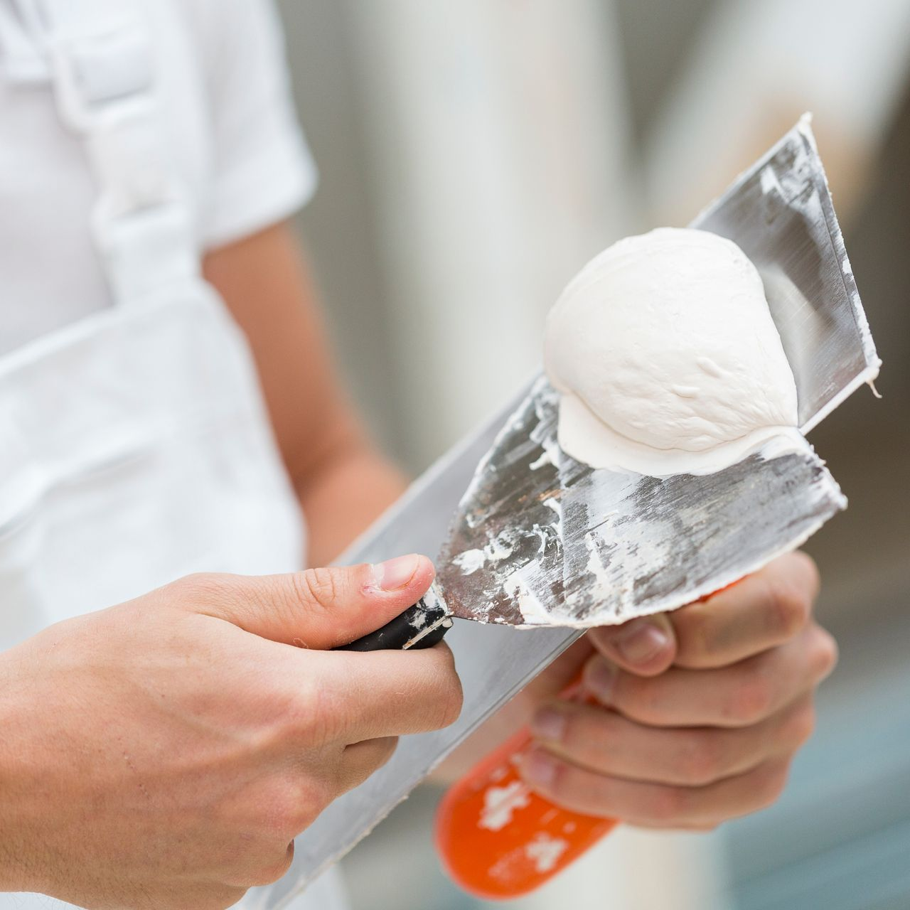 Personne tenant un couteau à mastic avec une noisette de plâtre blanc.