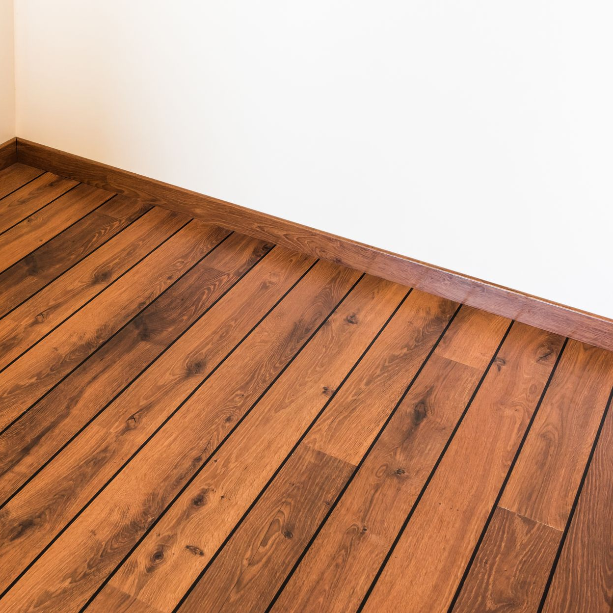 Un parquet brun contraste avec un mur blanc orné de plinthes brunes.