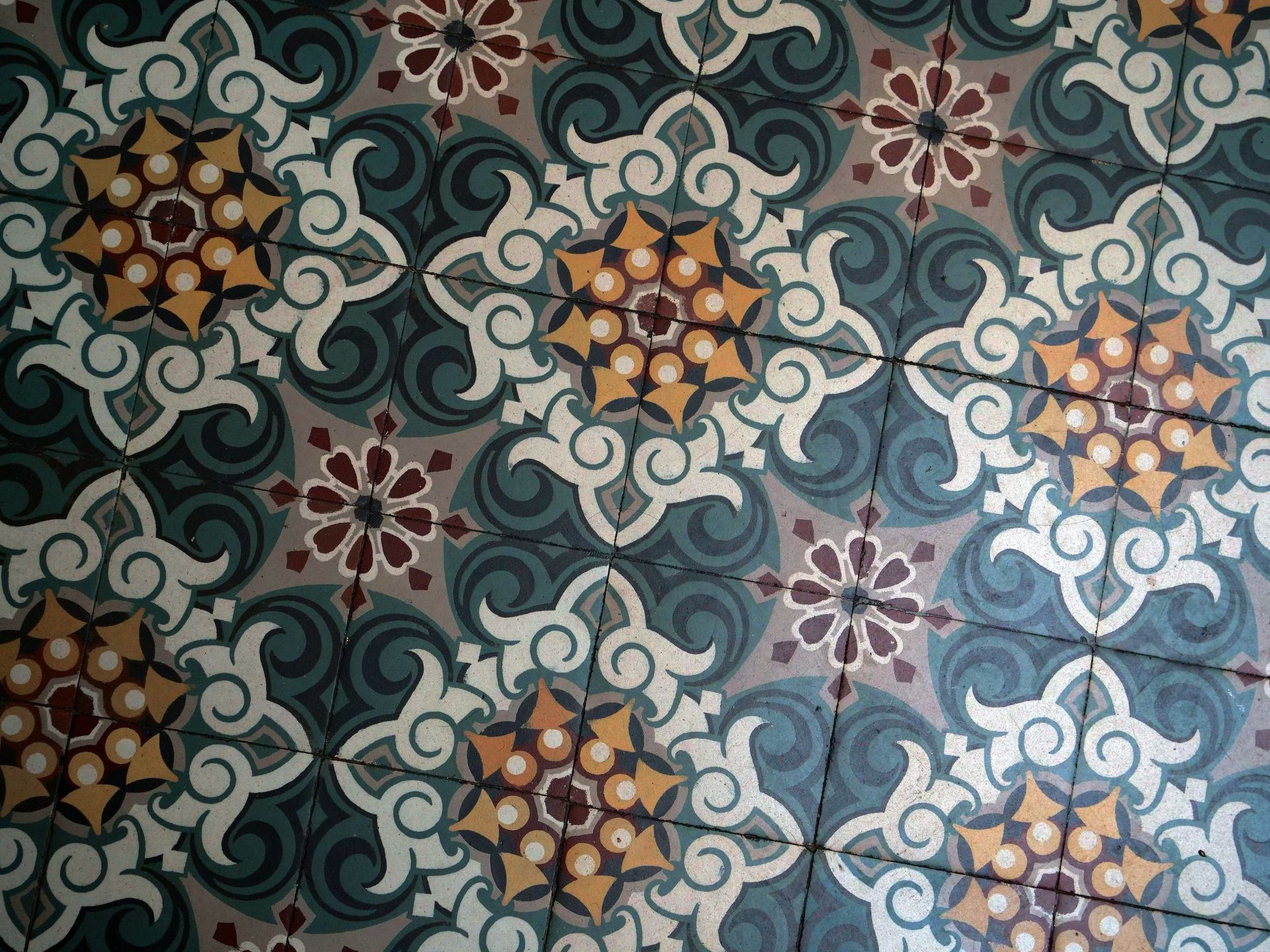 Carrelage décoratif au sol avec des motifs floraux et tourbillonnants répétitifs dans les tons turquoise, beige et marron.