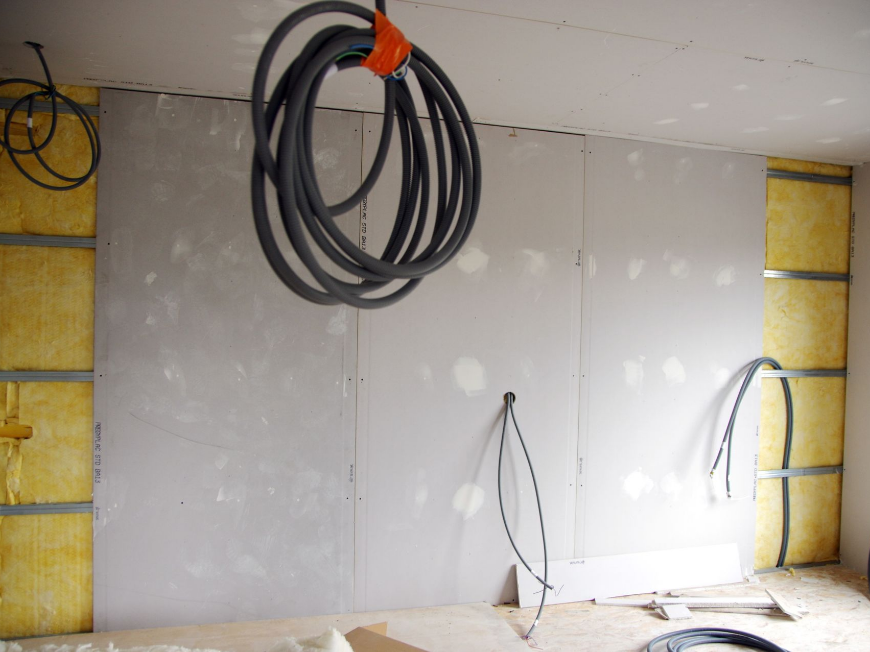 Mur intérieur en construction ; plaques de plâtre et isolant apparents. Câblage électrique visible.