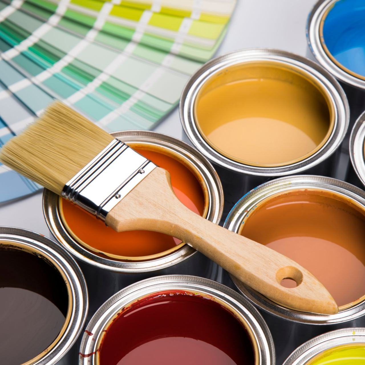 Un pinceau posé sur des pots de peinture de couleurs variées et des échantillons de couleurs en arrière-plan.