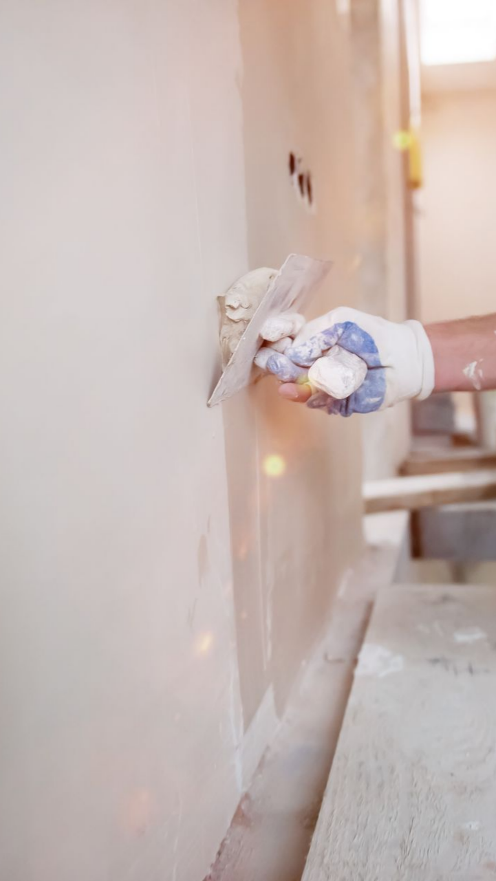 Personne portant un gant appliquant du plâtre sur un mur à l'aide d'une truelle.