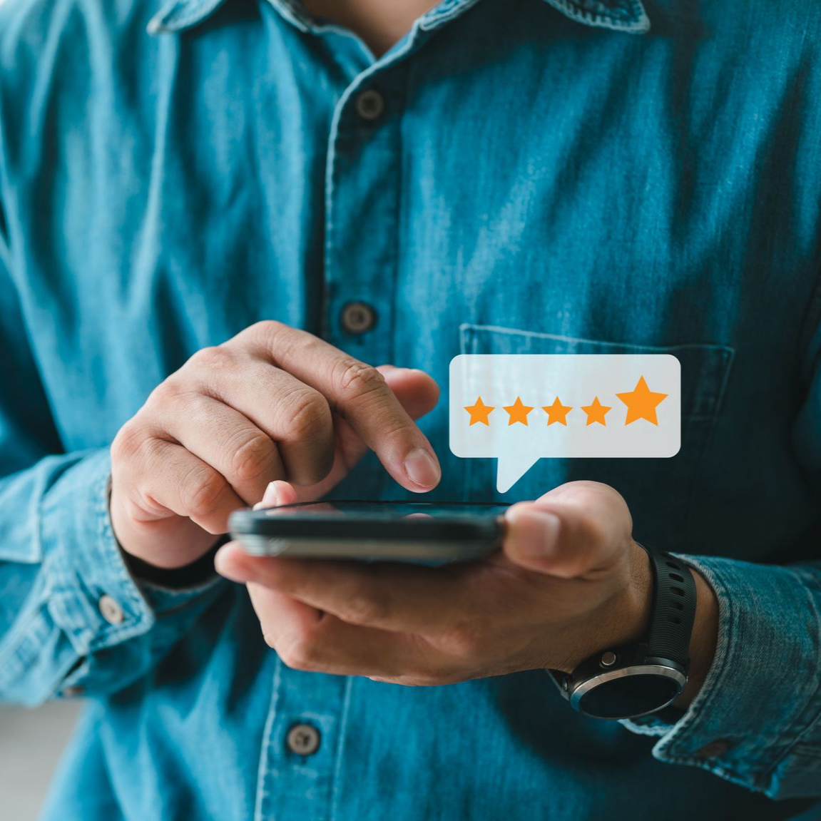 Une personne en chemise bleue, tenant son téléphone, attribue une note de cinq étoiles.