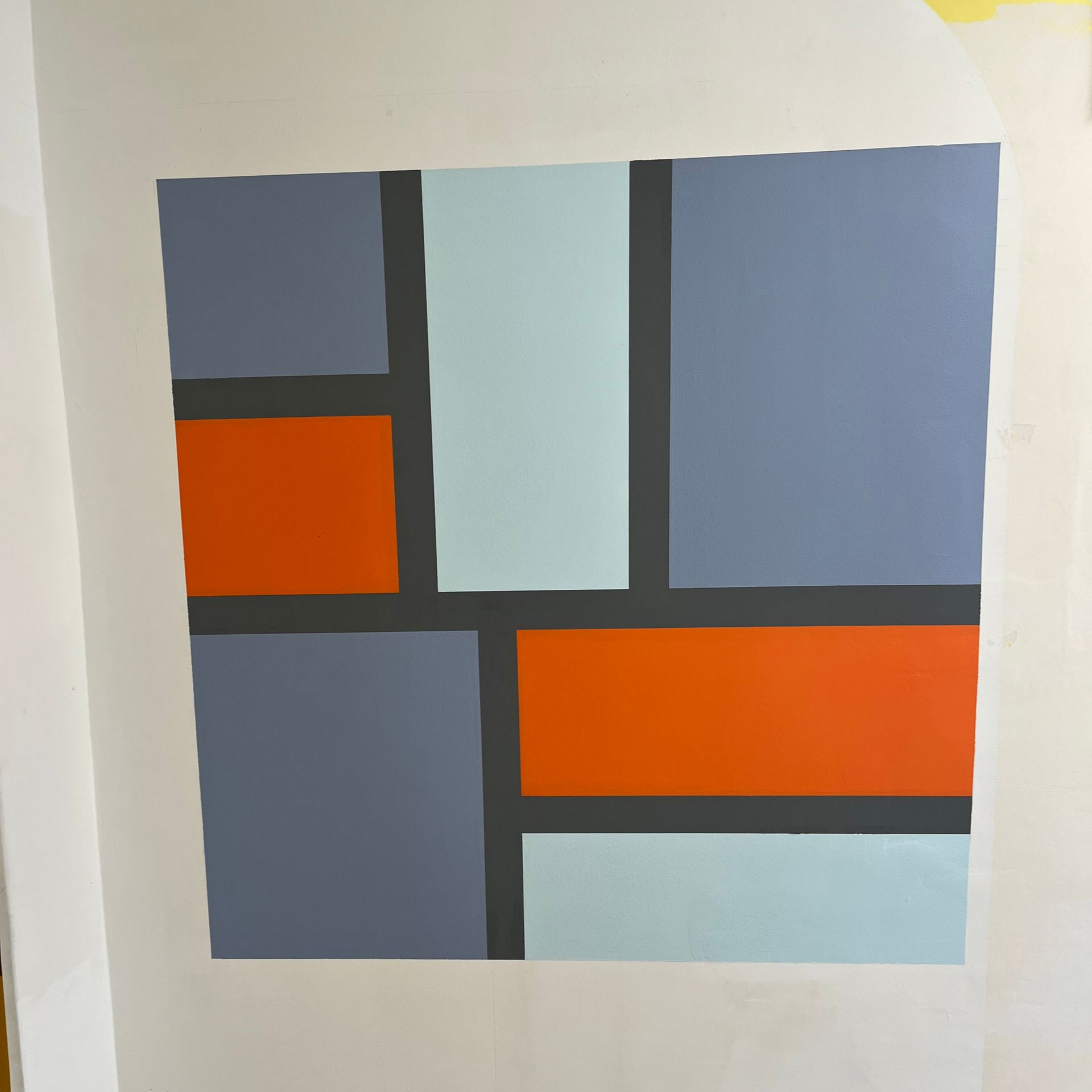 Œuvre d'art géométrique dans les tons de bleu, d'orange et de gris, avec des lignes noires, sur un mur blanc.