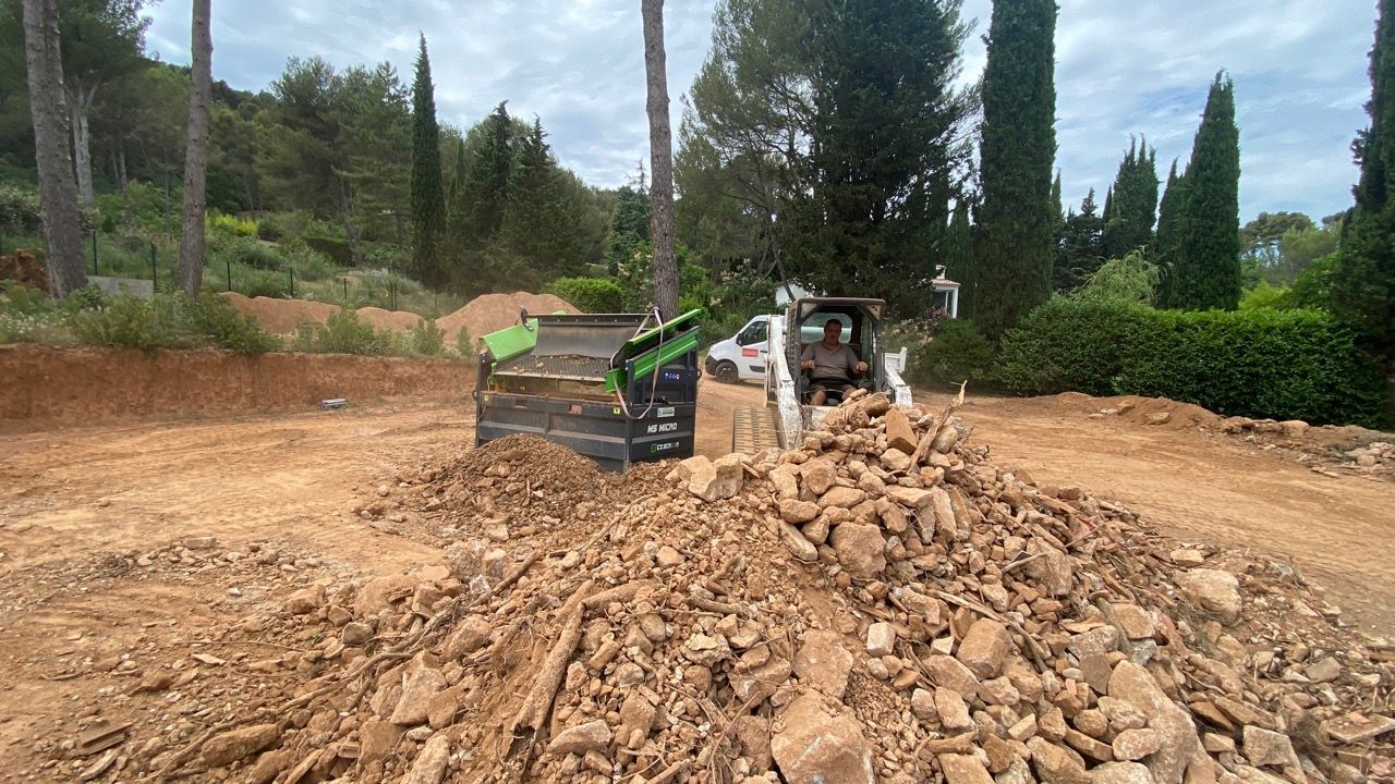 Une chargeuse compacte et une excavatrice déplacent des roches et de la terre sur un chantier extérieur.