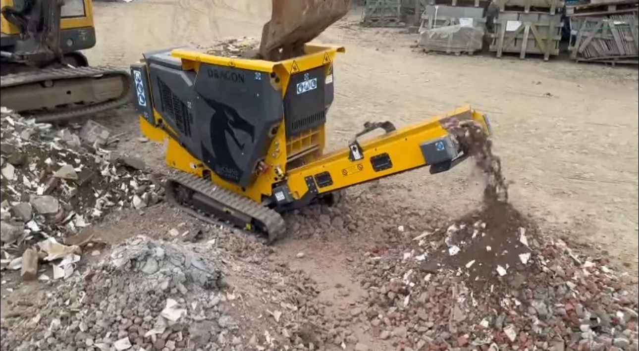 Concasseur de roches jaune avec convoyeurs, traitant un grand tas de roches en extérieur.
