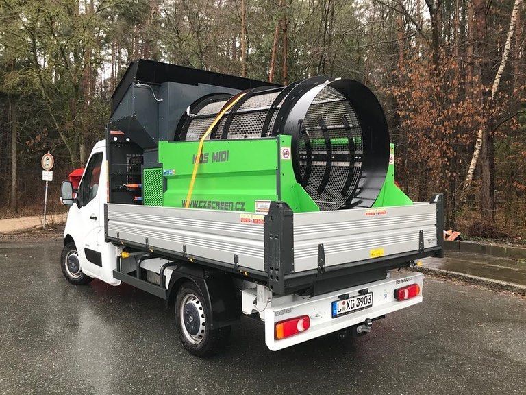Machine de criblage de terre verte à l'arrière d'un camion blanc, stationné sur une route.