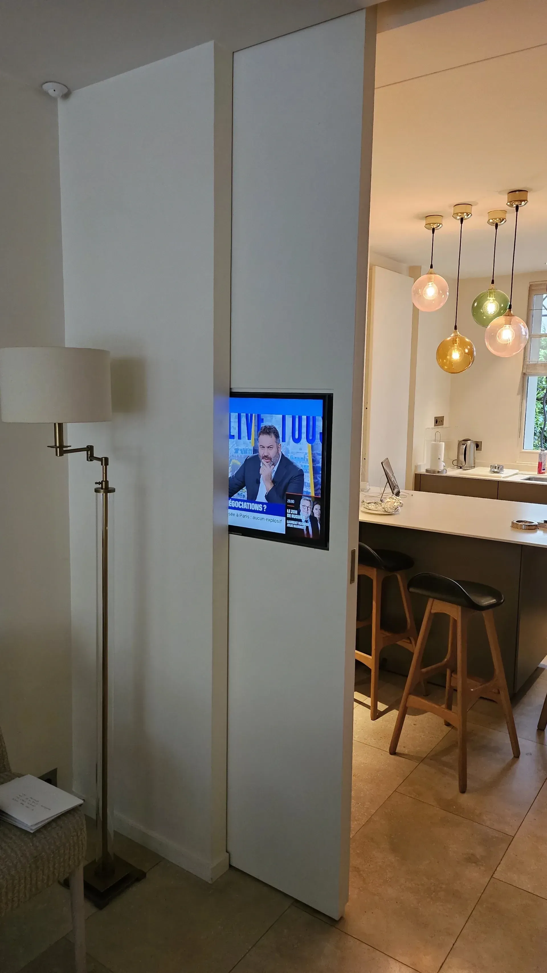 Salon avec une télévision murale et une vue dégagée sur une cuisine avec des suspensions et des tabourets