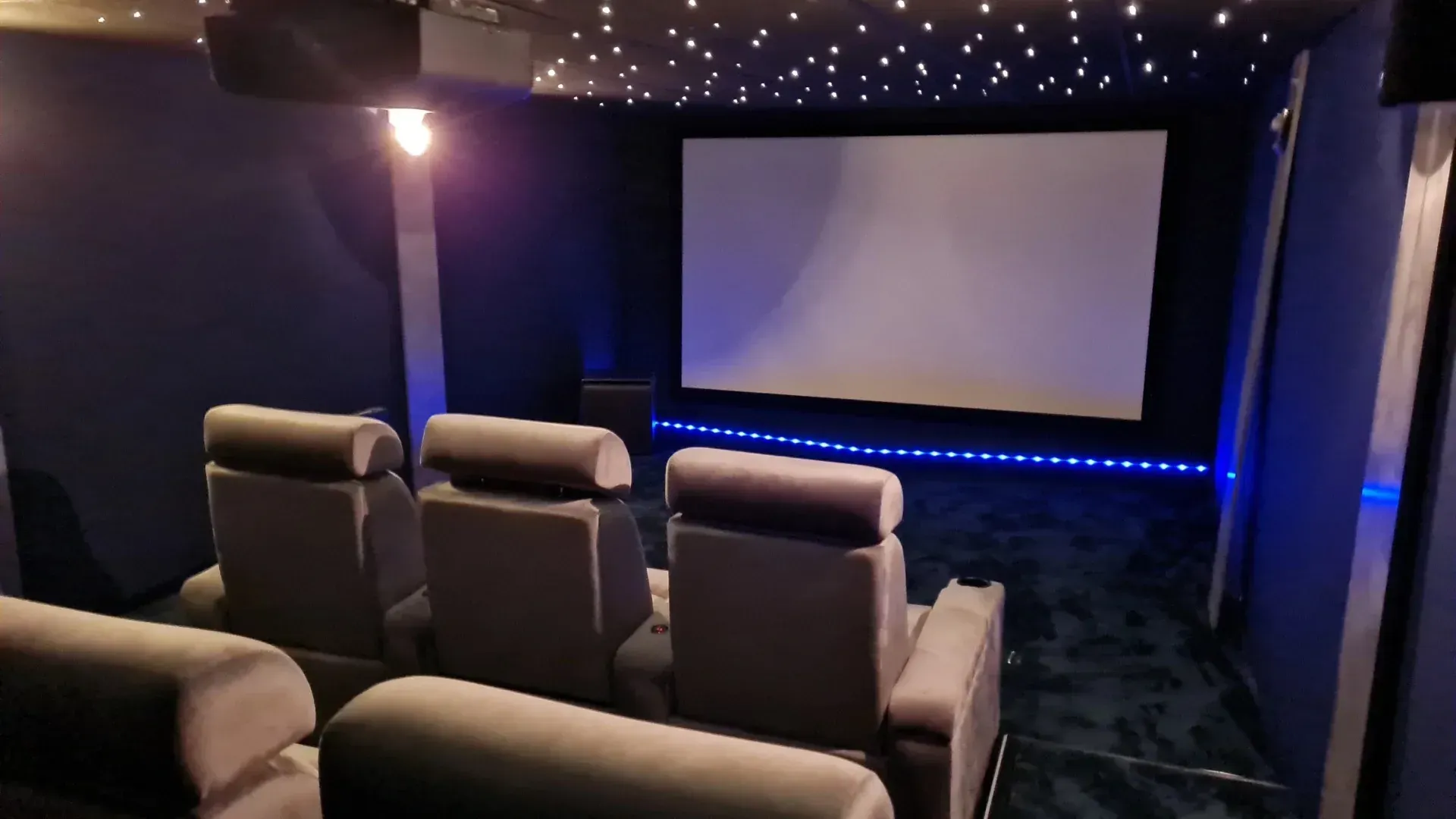 Petit home cinéma avec fauteuils inclinables, éclairage de plafond étoilé et grand écran de projection