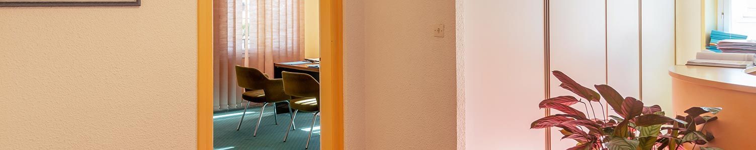 Vue depuis une pièce lumineuse sur un espace de bureau adjacent avec des encadrements de porte jaunes, un bureau, des chaises et une moquette verte.