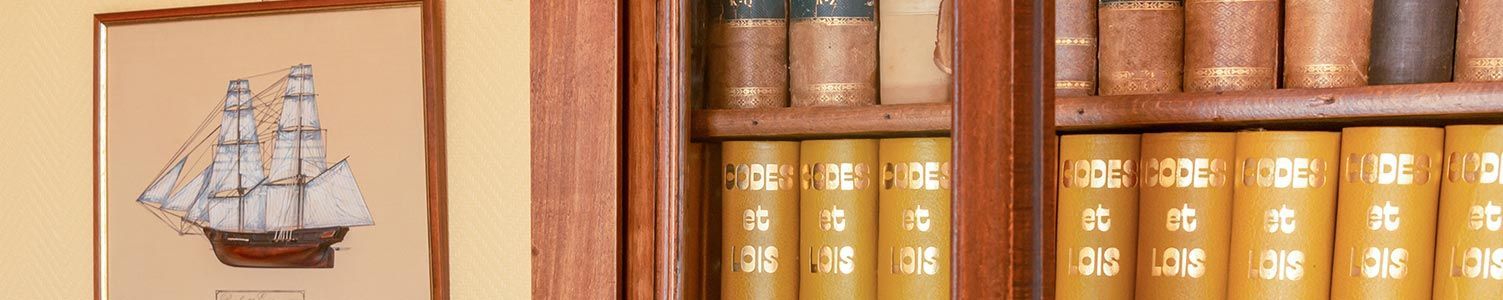 Un dessin encadré représentant un voilier est accroché au mur, à côté d'une bibliothèque en bois remplie de vieux livres reliés en cuir.