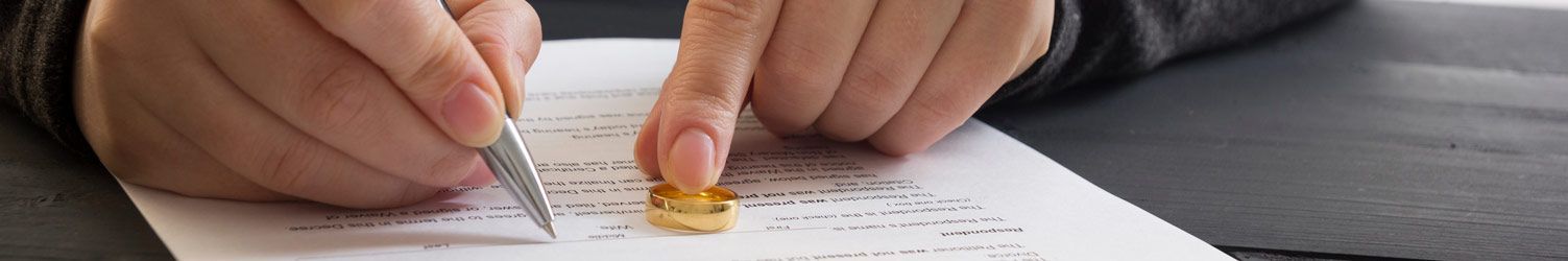Des mains tenant un stylo au-dessus d'un document, tandis qu'une alliance en or appuie contre le papier.