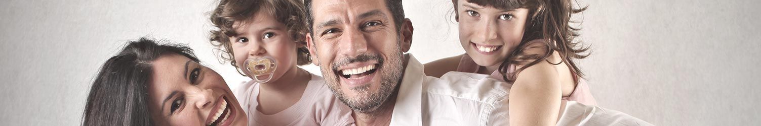 Une famille de quatre personnes souriantes, réunies dans un portrait en gros plan sur fond clair.