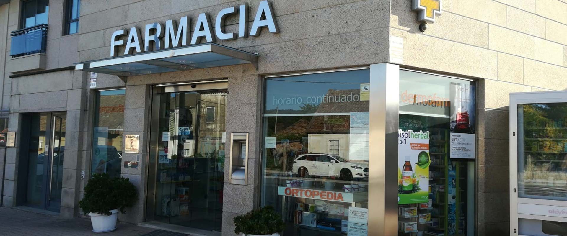 El frente de una farmacia con un coche aparcado delante.