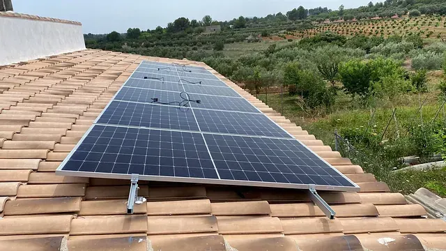 Paneles solares instalados sobre un tejado de tejas de terracota, con un olivar al fondo.