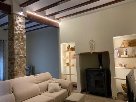 Sala de estar con columna de piedra, sofá, estanterías empotradas y chimenea. Combinación de colores neutros con vigas de madera y elementos decorativos.