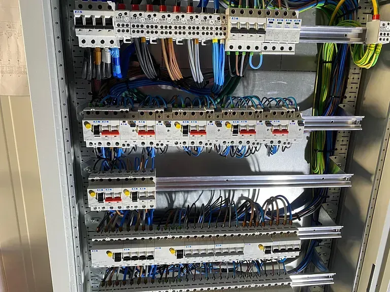 Panel eléctrico con filas de disyuntores y cables, que presenta una combinación de cables coloridos y de tonos neutros.