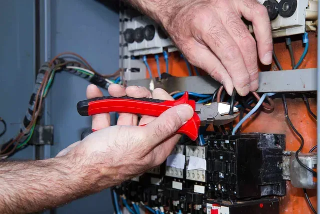 Manos utilizando alicates con mango rojo para trabajar con cables eléctricos dentro de un panel de control.