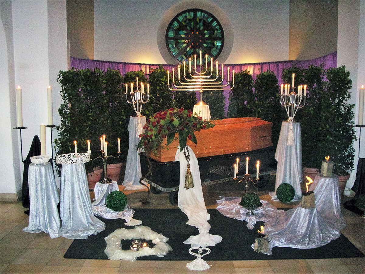 Ein Sarg ist in einer Kirche von Kerzen und Blumen umgeben