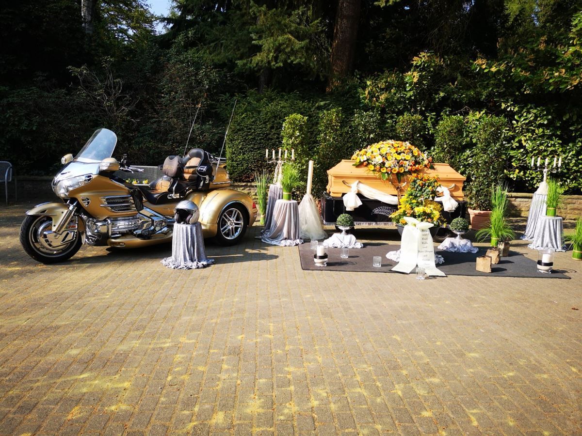 Ein Motorrad steht neben einem Sarg mit Blumen darauf